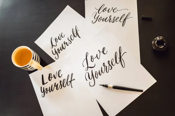 Love yourself. Calligrapher Young Woman writes phrase on white paper. Inscribing ornamental decorated letters. Calligraphy, graphic design, lettering, handwriting, creation concept