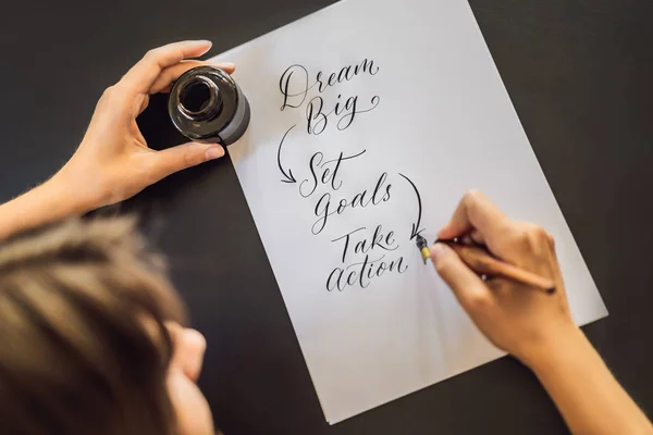 dream big set goals take action. Calligrapher Young Woman writes phrase on white paper. Inscribing ornamental decorated letters. Calligraphy, graphic design, lettering, handwriting, creation concept