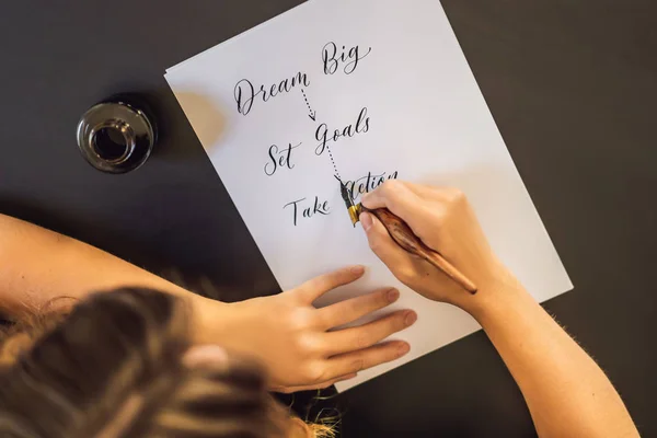 dream big set goals take action. Calligrapher Young Woman writes phrase on white paper. Inscribing ornamental decorated letters. Calligraphy, graphic design, lettering, handwriting, creation concept