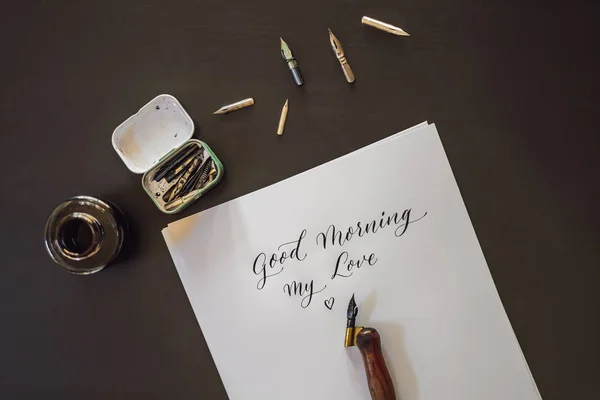 Jó reggelt. Kalligráfus fiatal nő írja mondat a fehér papíron. Inscribing díszes díszített leveleket. Kalligráfia, grafikai tervezés, betűk, kézírás, létrehozás koncepció — Stock Fotó