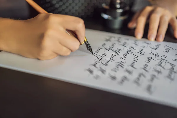 Calígrafo manos escribe frase en papel blanco. Frase bíblica sobre el amor Inscripción de letras ornamentales decoradas. Caligrafía, diseño gráfico, letras, escritura a mano, concepto de creación — Foto de Stock