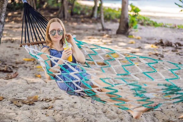 Mujer joven en la playa en una hamaca con una bebida —  Fotos de Stock