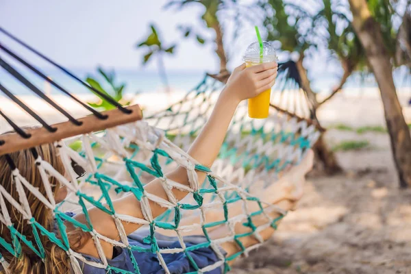 Mujer joven en la playa en una hamaca con una bebida —  Fotos de Stock