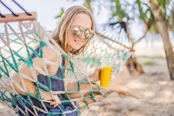 Mujer joven en la playa en una hamaca con una bebida —  Fotos de Stock