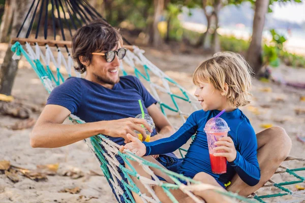 Papá y su hijo se divierten en una hamaca con una bebida — Foto de Stock