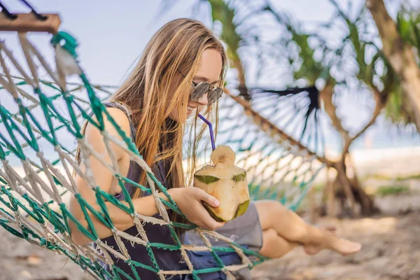 Mujer joven en la playa en una hamaca con una bebida —  Fotos de Stock