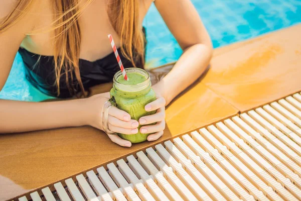 Woman with a green smoothies of spinach and banana on the background of the pool. Healthy food, healthy smoothies
