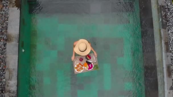 Аэросъемка молодой туристки с собственным завтраком на плавучем столе в частном бассейне — стоковое видео