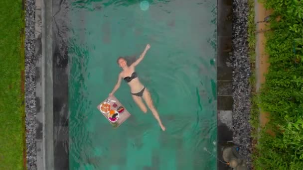 Foto aerea di una giovane turista che fa la sua colazione personale su un tavolo galleggiante in una piscina privata — Video Stock