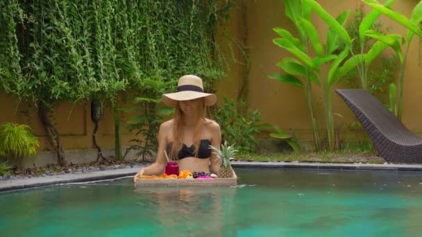 Una joven turista tiene su propio desayuno personal en una mesa flotante en una piscina privada. Estilo de vida de playa tropical — Vídeos de Stock
