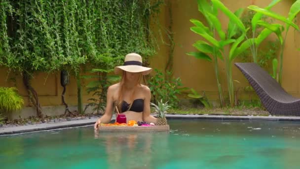一位年轻女游客在私人游泳池的浮动桌子上享用自己的个人早餐。热带海滩生活方式 — 图库视频影像