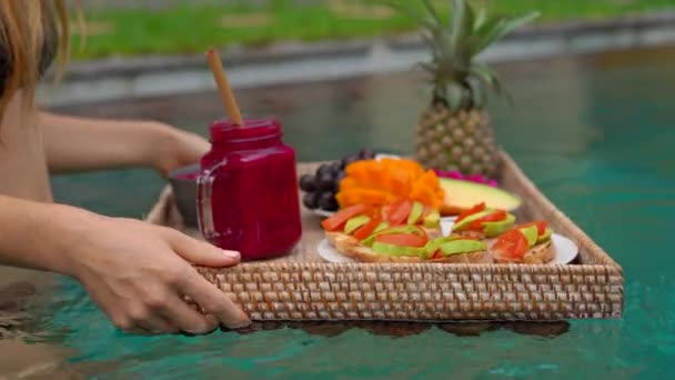 Een jonge vrouw toerist heeft haar eigen persoonlijke Ontbijt op een drijvende tafel in een prive-zwembad. Tropical Beach Lifestyle — Stockvideo