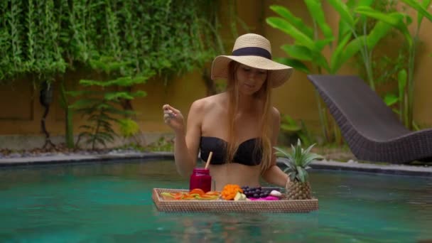 A young woman tourist has her own personal breakfast on a floating table in a private swimming pool. Tropical beach lifestyle — Stock Video