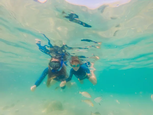 Счастливая мать и сын ныряют с маской в море. Посмотри на рыбу под водой. — стоковое фото
