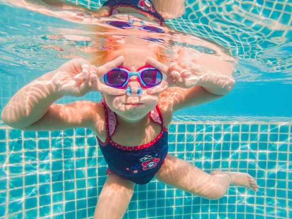 La bambina nel parco acquatico nuota sott'acqua e sorride — Foto Stock