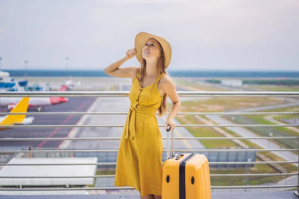 Começa a sua jornada. Linda jovem viajante em um vestido amarelo e uma mala amarela está esperando por seu voo — Fotografia de Stock