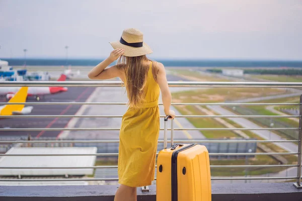 Start of her journey. Beautiful young woman ltraveler in a yellow dress and a yellow suitcase is waiting for her flight — Stock Photo, Image