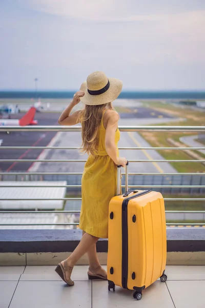 Rozpoczęcie podróży. Piękna młoda kobieta ltraveler w żółtej sukni i żółta walizka czeka na jej lot — Zdjęcie stockowe
