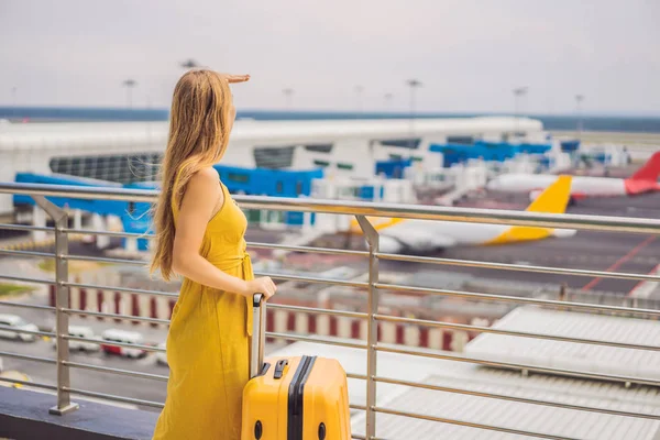 ' Ρχισε το ταξίδι της. Όμορφη νεαρή γυναίκα με ένα κίτρινο φόρεμα και μια κίτρινη βαλίτσα περιμένει την πτήση της — Φωτογραφία Αρχείου
