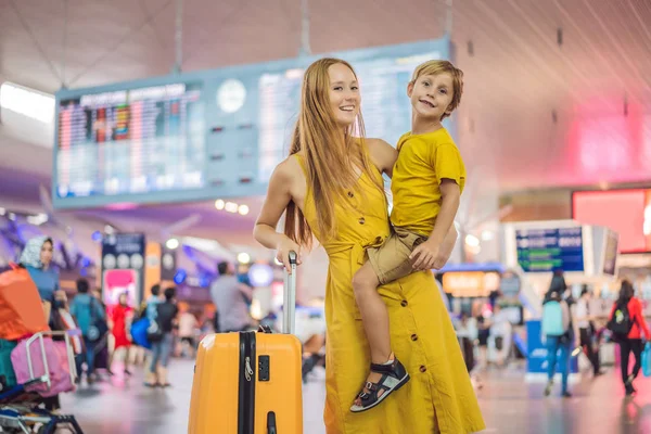 Family at airport before flight. Mother and son waiting to board at departure gate of modern international terminal. Traveling and flying with children. Mom with kid boarding airplane. yellow family