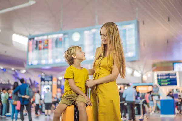 Family at airport before flight. Mother and son waiting to board at departure gate of modern international terminal. Traveling and flying with children. Mom with kid boarding airplane. yellow family