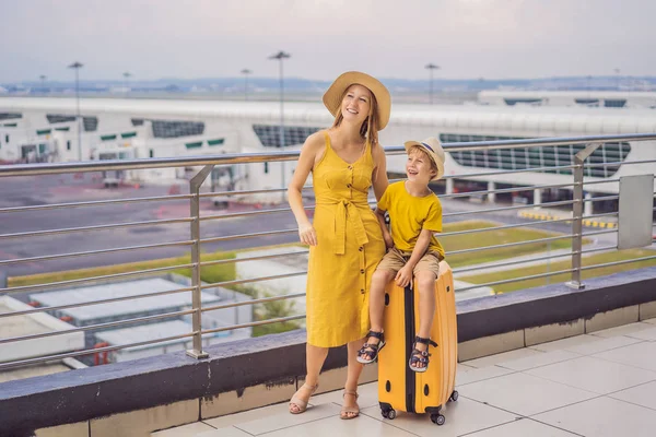 Family at airport before flight. Mother and son waiting to board at departure gate of modern international terminal. Traveling and flying with children. Mom with kid boarding airplane. yellow family