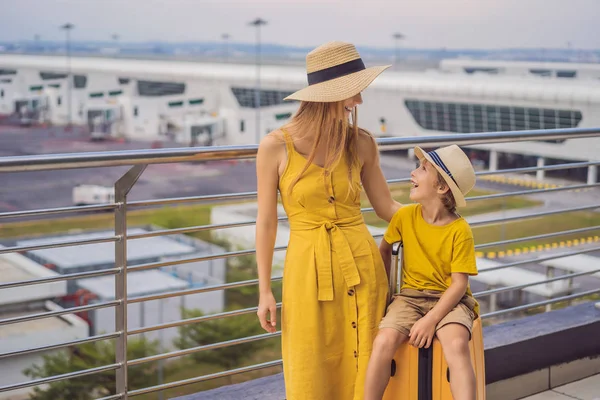 Family at airport before flight. Mother and son waiting to board at departure gate of modern international terminal. Traveling and flying with children. Mom with kid boarding airplane. yellow family