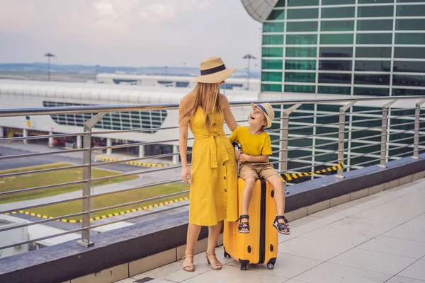 Family at airport before flight. Mother and son waiting to board at departure gate of modern international terminal. Traveling and flying with children. Mom with kid boarding airplane. yellow family