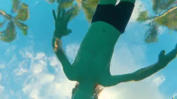 Pohled ze spodní části bazénu na palmami a malé dítě, které plaví přes kameru — Stock video