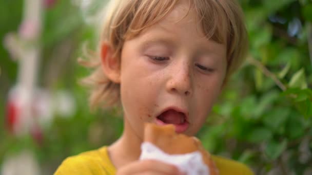 Closeup shot of a little boy eating a tasty pancake on a street market. Street food concept. — Stock Video