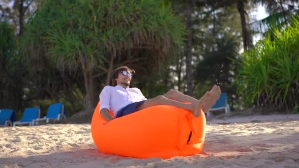 Молодий чоловік на тропічному пляжі лежав на надувному дивані, який він щойно надув. Концепція літніх канікул — стокове відео