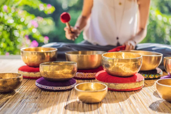 Frau spielt auf tibetischer Klangschale, während sie auf einer Yogamatte gegen einen Wasserfall sitzt. Jahrgangstonnen. schöne Mädchen mit Mala-Perlen meditieren — Stockfoto