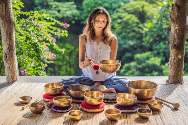 Kvinna spelar på tibetanska sjungande skål medan du sitter på yogamattan mot ett vattenfall. Vintage tonned. Vacker flicka med mala pärlor mediterar — Stockfoto