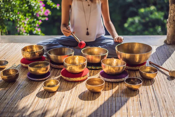 Kvinna spelar på tibetanska sjungande skål medan du sitter på yogamattan mot ett vattenfall. Vintage tonned. Vacker flicka med mala pärlor mediterar — Stockfoto