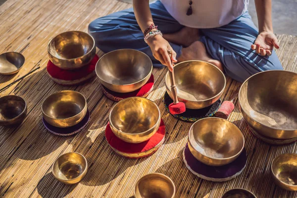 Frau spielt auf tibetischer Klangschale, während sie auf einer Yogamatte gegen einen Wasserfall sitzt. Jahrgangstonnen. schöne Mädchen mit Mala-Perlen meditieren — Stockfoto