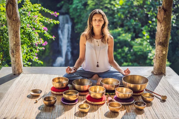 Vrouw spelen op Tibetaanse Singing Bowl terwijl zittend op yoga mat tegen een waterval. Vintage tonned. Mooi meisje met Mala kralen mediteren — Stockfoto