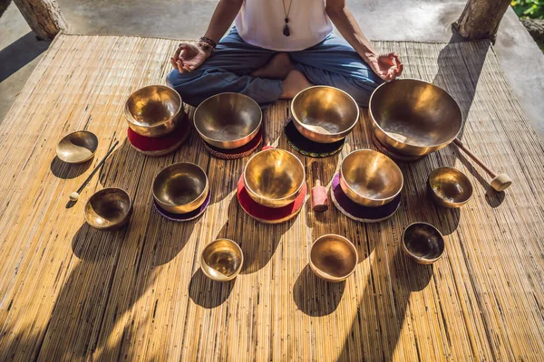 Frau spielt auf tibetischer Klangschale, während sie auf einer Yogamatte gegen einen Wasserfall sitzt. Jahrgangstonnen. schöne Mädchen mit Mala-Perlen meditieren — Stockfoto