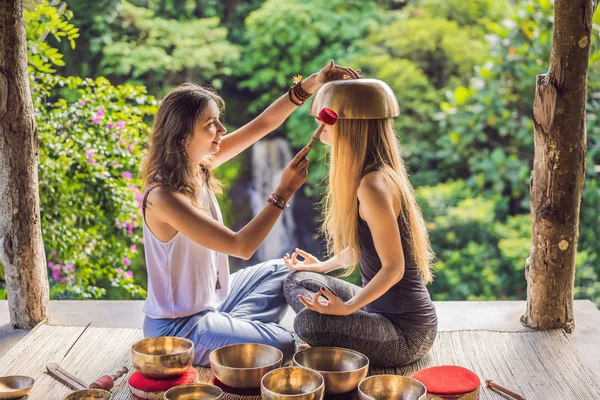 Nepal Buddha copper singing bowl at spa salon. Young beautiful woman doing massage therapy singing bowls in the Spa against a waterfall. Sound therapy, recreation, meditation, healthy lifestyle and