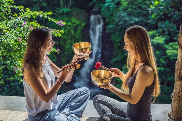 Nepal Buda tigela de cobre cantando no salão de spa. Jovem mulher bonita fazendo massagem terapia cantando tigelas no Spa contra uma cachoeira. Terapia sonora, recreação, meditação, estilo de vida saudável e — Fotografia de Stock