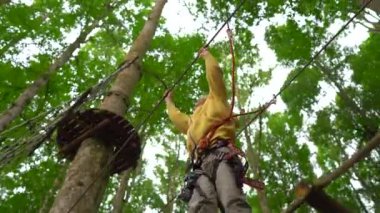 Bir güvenlik koşum küçük çocuk bir orman macera parkı ağaç tepelerinde bir rota üzerinde tırmanıyor. Yüksek halat patikalarına tırmanıyor. Zip hatları ve tüm oluşan tırmanma faaliyetleri ile açık eğlence merkezi