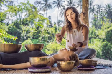 Spa salonunda Nepal Buda bakır kasesi. Genç, güzel bir kadın masaj terapisi yapıyor. Spa 'da şelaleye karşı kâseler söylüyor. Ses terapisi, dinlenme, meditasyon, sağlıklı yaşam tarzı ve...