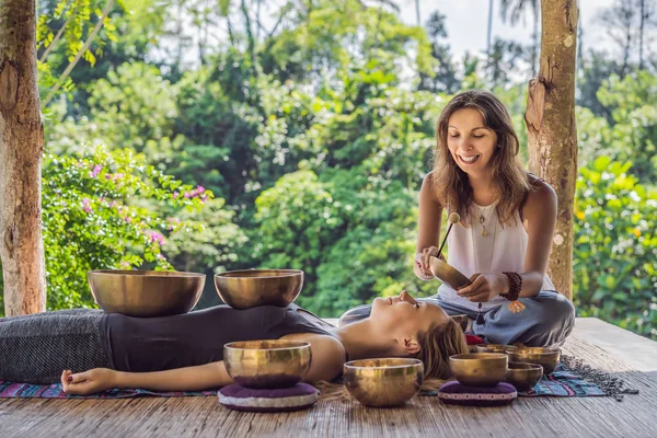 Nepal Cuenco de cobre de Buda en el salón de spa. Joven hermosa mujer haciendo terapia de masaje cantando cuencos en el Spa contra una cascada. Terapia de sonido, recreación, meditación, estilo de vida saludable y —  Fotos de Stock