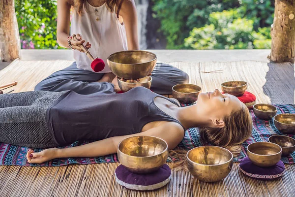 Nepal Buddha koppar sång skål på spa salong. Ung vacker kvinna som gör massage terapi sjunga skålar i Spa mot ett vattenfall. Ljudterapi, rekreation, meditation, hälsosam livsstil och — Stockfoto