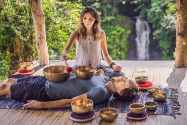 Spa salonunda Nepal Buda bakır şarkı kase. Genç güzel adam bir şelale karşı Spa'da şarkı kase masaj terapisi yapıyor. Ses terapisi, rekreasyon, meditasyon, sağlıklı yaşam tarzı ve vücut