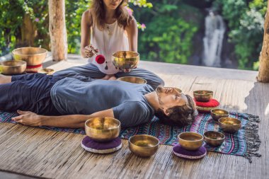 Spa salonunda Nepal Buda bakır şarkı kase. Genç güzel adam bir şelale karşı Spa'da şarkı kase masaj terapisi yapıyor. Ses terapisi, rekreasyon, meditasyon, sağlıklı yaşam tarzı ve vücut