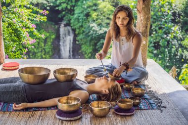 Spa salonunda Nepal Buda bakır kasesi. Genç, güzel bir kadın masaj terapisi yapıyor. Spa 'da şelaleye karşı kâseler söylüyor. Ses terapisi, dinlenme, meditasyon, sağlıklı yaşam tarzı ve...