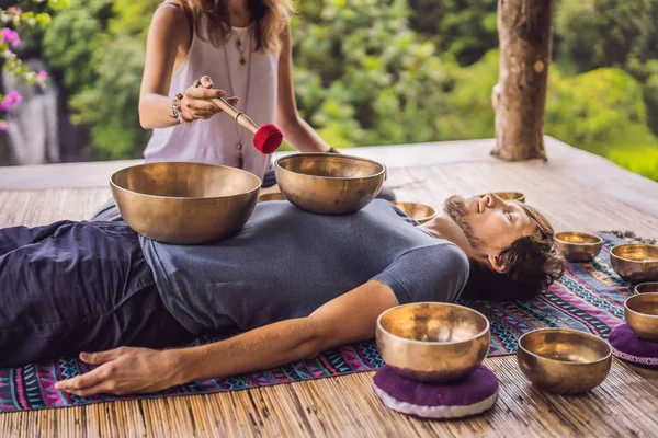 Nepal Cuenco de cobre de Buda en el salón de spa. Joven hombre hermoso haciendo terapia de masaje cantando cuencos en el Spa contra una cascada. Terapia de sonido, recreación, meditación, estilo de vida saludable y cuerpo —  Fotos de Stock