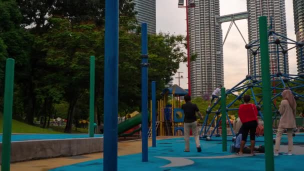 Plan de Tymelapse du parc central de Kuala Lumpur avec vue sur les tours Petronas et l'aire de jeux pour enfants au premier plan — Video