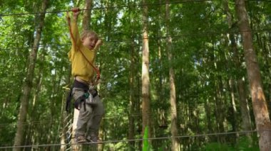 Bir güvenlik koşum küçük çocuk bir orman macera parkı bir rota üzerinde tırmanıyor. Yüksek halat patikalarına tırmanıyor. Zip hatları ve her türlü oluşan tırmanma faaliyetleri ile açık eğlence merkezi