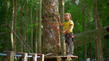Superslowmotion bir orman macera parkı bir rota üzerinde bir güvenlik koşum küçük bir çocuk çekim. Zip hatları ve her türlü engellerden oluşan tırmanma faaliyetleri ile açık eğlence merkezi